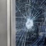 Que Faire en Cas de Vitre Cassée à Anderlecht ? : Fenêtre résidentielle brisée à Anderlecht avec verre au sol, nécessitant une intervention d'urgence.