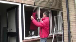 Vitrier professionnel retirant un vieux simple vitrage pour installer un double vitrage HR++ sur un châssis en bois conservé à Anderlecht.
